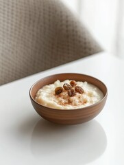 A bowl of creamy rice pudding topped with raisins and cinnamon, placed on a white table.