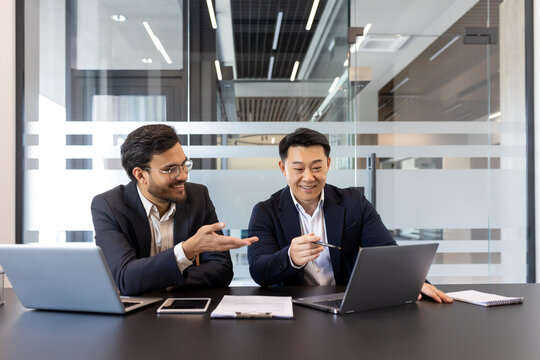 Two businessmen are engaged in a collaborative meeting in a contemporary office setting. They are using laptops and documents, creating a dynamic and professional atmosphere for business planning