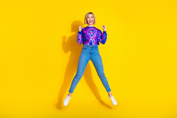 Full length photo of lovely young lady jump winning have fun dressed stylish colorful blue garment isolated on yellow color background
