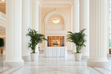 Colonnade, A spacious, elegant lobby features tall columns, potted plants, and a floral display on a white table, creating a luxurious ambiance.