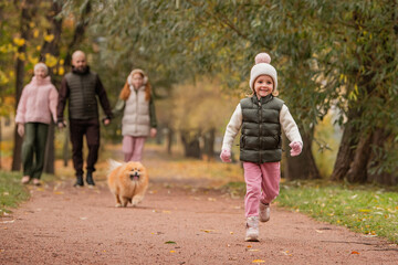 Obraz premium A little girl and her pet Pomeranian run along a path in an autumn city park.