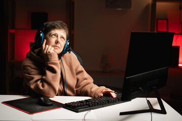 Thoughtful woman with headphones contemplating next step in eSports tournament playing online at...