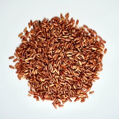 Pile of uncooked raw brown red rice or beras merah food ingredients isolated on square white background from above angle view.