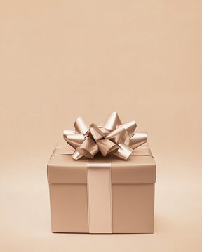 A beige gift box with a large metallic bow on top, against an isolated light brown background. Front view.Christmas, Valentine and birthday card