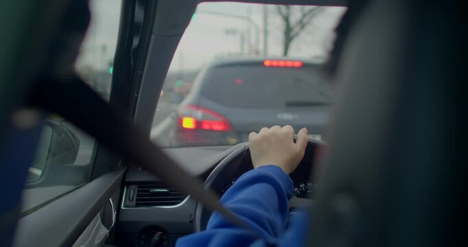 A view inside a car shows hands gripping the steering wheel while watching the traffic ahead
