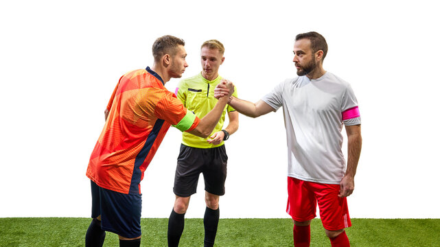 Two serious men, soccer players from opposite team, standing next to referee and shaking hands isolated on white background. Concept of sport, fair play, competition, control, rules
