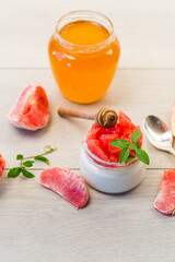 homemade sweet yogurt in a glass jar with pieces of red ripe grapefruit and honey, on a wooden table