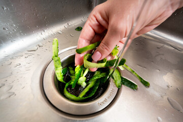Disposing of fresh vegetable peelings in a kitchen sink garbage disposer under running water.
