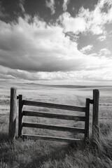 Fototapeta premium Gate is open in a field with a cloudy sky in the background. The gate is wooden and has a rustic appearance. The scene is peaceful and serene, with the gate serving as a gateway to the open field