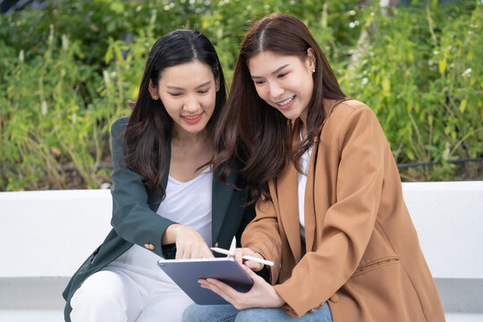 Two Asian businesswomen use a digital Tablet to collaborate remote work. Work from anywhere empowers the lady to balance professional and personal goals.