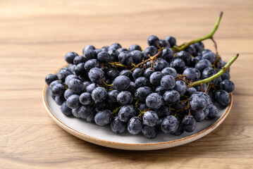 Black grapes on plate with wooden table, Seedless grapes