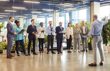 Multicultural group of businessmen standing in a row in a hotel lobby. Employees listen to the...