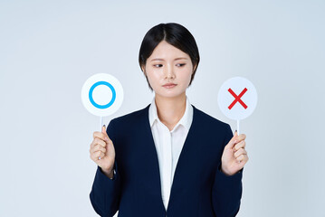 マルとバツのプレートを持つスーツ姿の女性