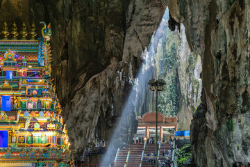 Naklejka premium Batu Caves interior with main Hindu Temple, Selangor, Malaysia. Tourists visiting Batu cave complex illuminated by natural light streaming through the cave's opening, Kuala Lumpur
