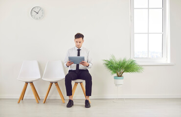 Man is waiting for a job interview in an empty office, sitting on a chair. The candidate is prepared for business work, representing a professional atmosphere in a corporate setting.