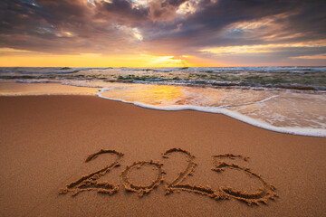 Happy New Year 2025 text lettering on the beach sand at sunrise