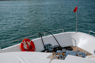 Bow of a yacht with a red lifeboat, anchor ropes, metal structures and a waving flag on the stern,...