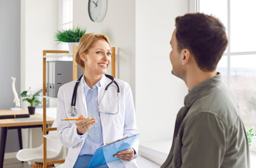 Fototapeta premium Portrait of a young sick man patient sitting in medical office listening to a friendly female doctor holding report file with appointment and giving consultation during medical examination in clinic.
