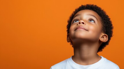 A young boy with brown hair and a white shirt is looking up at the sky. The boy is smiling and he is in a good mood. The orange background adds a warm and inviting atmosphere to the scene
