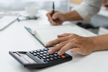 accountant reviews financial data using a calculator at desk in a busy office, ensuring accuracy in tax reporting and financial management.