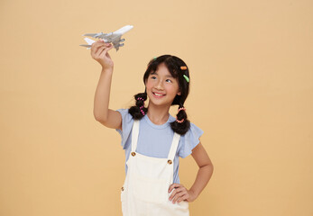 Happy Smiling Asian child playing toy plane going on summer holiday travel isolated on nude color background. Vacation concept