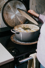 A person is cooking food in a pot with a lid on top. The pot is filled with vegetables and herbs, and the lid is on top of it