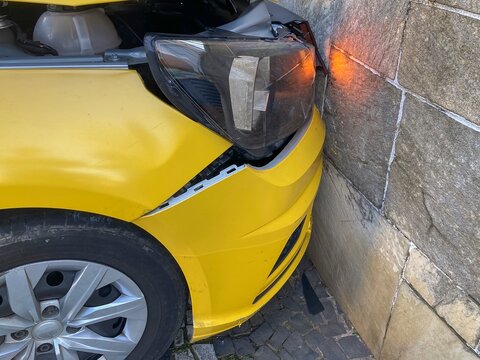 Yellow car crashed into wall. Hood, front end and fender crushed into stone wall.