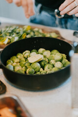 A black pot filled with green vegetables, including broccoli. A person is standing behind the pot. Scene is that of a person cooking or preparing food