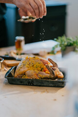 A person is seasoning a turkey in a pan. The turkey is covered in a mixture of herbs and spices