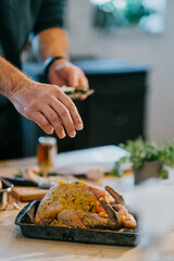 A man is seasoning a turkey on a table. The turkey is placed in a pan and the man is sprinkling salt on it