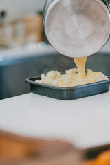 A pot of food is being poured into a pan. The pan is black and the food is yellow