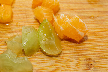 Detalle de trozos de mandarina y uvas verdes sobre una tabla de madera con textura natural