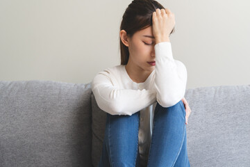 Unhappy anxiety young Asian woman covering her face with pillow on the cough in the living room at home.