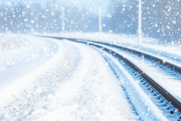 A serene winter scene featuring a snow-covered railway track winding through a snowy landscape. Soft snowflakes are falling, creating a tranquil atmosphere.