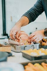 A man is preparing a roast in a pan. The pan is on a table with other food items
