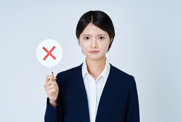 バツが描かれたプレートを持つスーツ姿の女性