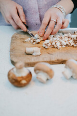 A woman is cutting mushrooms on a wooden cutting board. The mushrooms are sliced into small pieces. Concept of preparation for a meal