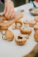 A person is cutting mushrooms on a cutting board. The mushrooms are in various stages of preparation, with some already cut and others still whole. Concept of anticipation and preparation for a meal