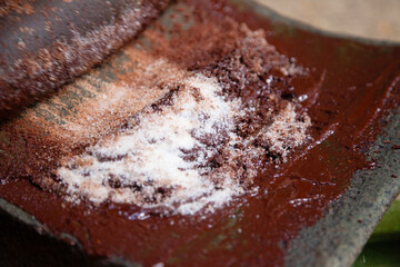 A woman in Oaxaca Mexico manually producing organic chocolate on a metate, an ancient stone tool for grinding food products.