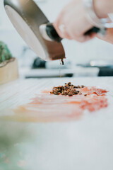 A person is pouring something into a pan. The pan is on a table. The person is wearing a ring