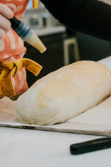 A person is making a bread roll with a brush. The roll is on a baking sheet. The person is wearing an apron
