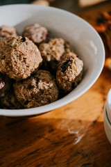A bowl of cookies sits on a wooden table. The cookies are small and round, and they are all different colors. The bowl is almost empty, with only a few cookies left. Scene is cozy and inviting