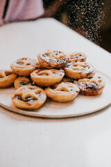 A plate of pastries with powdered sugar on top. The plate is white and the pastries are yellow