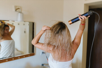 Young woman drying her hair with a styler, a hair dryer at home