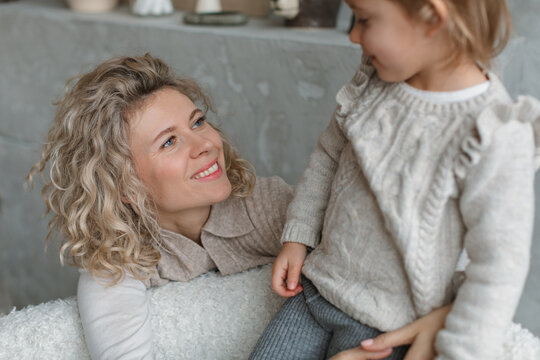 Close-up of a young girl sitting on the back of a sofa with her mother hugging her from behind