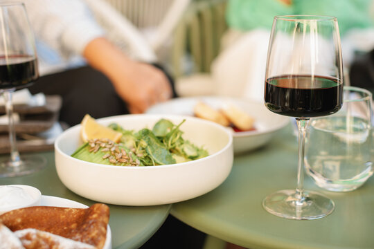 Close-up of an avocado, lettuce, cucumber and sunflower seed salad on a cafe table with a glass of red wine