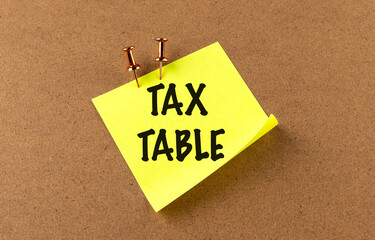 Tax table concept with handwritten text on a yellow sticky note pinned to a corkboard background