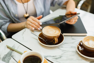 Close-up of a woman working on a digital tablet while drinking coffee on the cafe terrace.