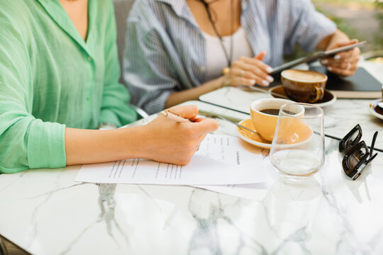Two young women discussing work processes, signing documents and drinking coffee at a cafe