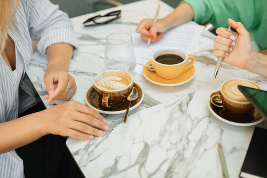 Three young women discussing work processes, signing documents and drinking coffee at a cafe